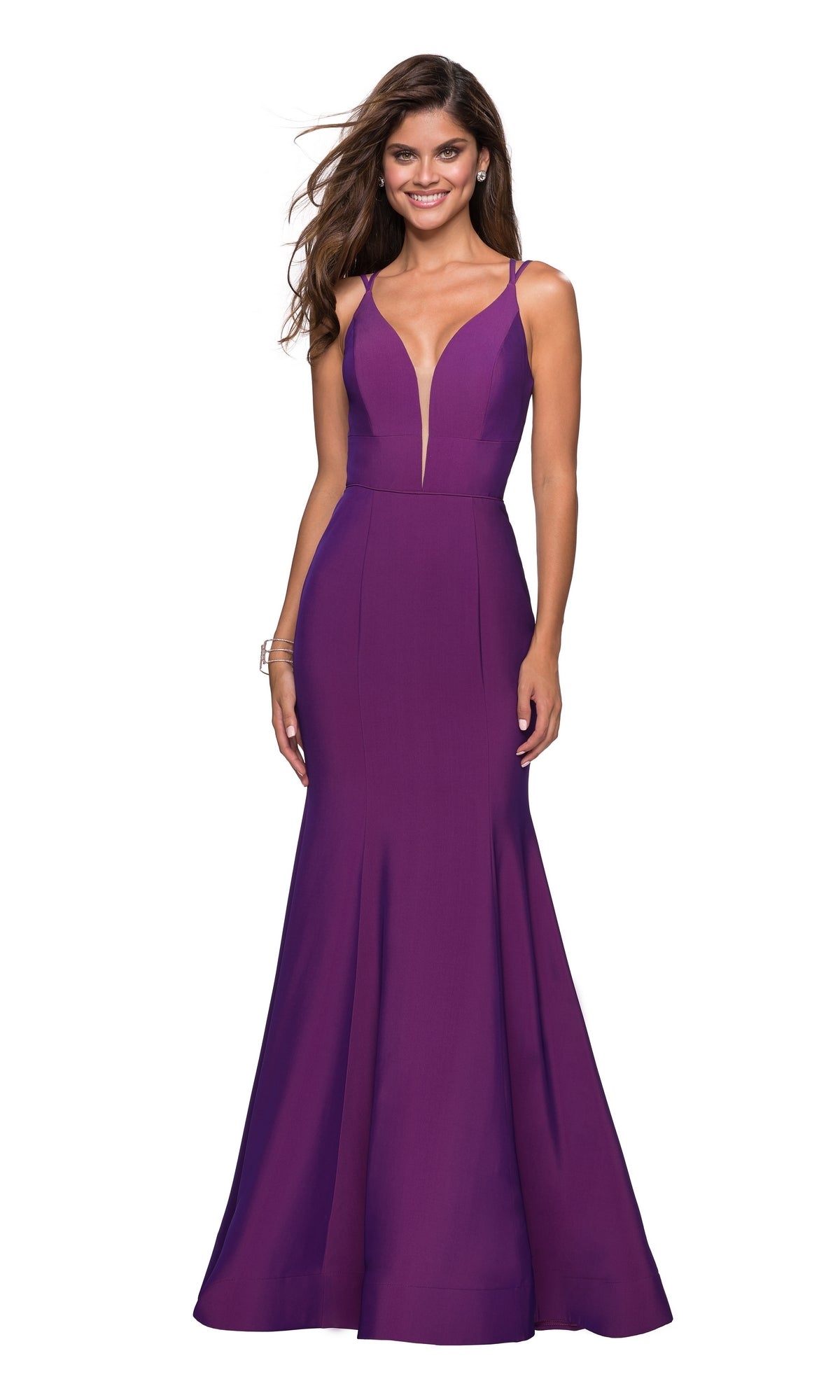 A woman wears the La Femme Open-Back V-Neck Jersey Prom Dress 27446, a sleeveless deep purple mermaid gown with double spaghetti straps and an open back, standing against a white background.